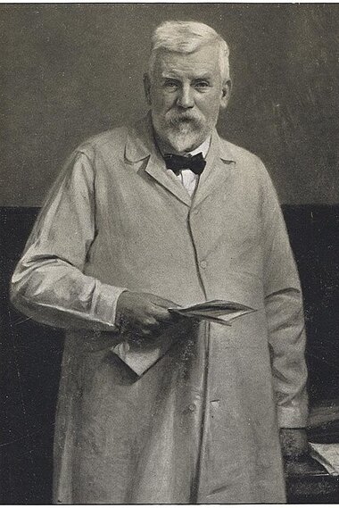 Black and white photo of an elderly man with a beard, wearing a suit and holding a book.