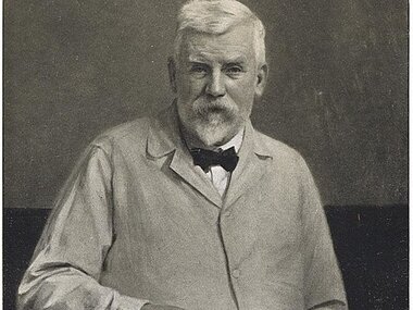 Black and white photo of an elderly man with a beard, wearing a suit and holding a book.