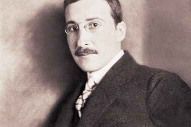 Black and white photograph of a man with glasses and a mustache, posing in a suit.