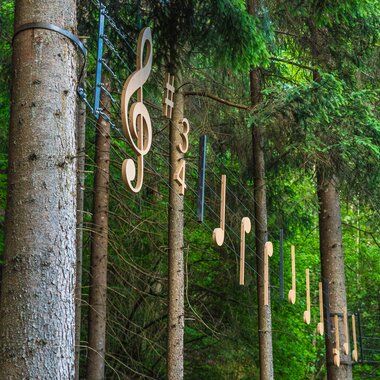 Sound sculpture with music notes attached to trees in a forest.