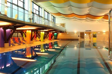 Interior of a modern indoor swimming pool with a retractable roof and colorful ceiling design. | © Freges