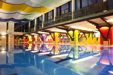 Interior of a modern swimming pool with colorful lighting, loungers, and an upper balcony. | © Johannes Felsch