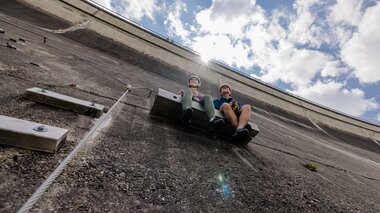 Two climbers resting on a ladder on a steep wall with clouds in the sky above. | © Zell am See-Kaprun Tourismus