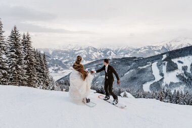 A wedding couple snowboarding in a snowy winter landscape with mountains in the background. | © Wild Connections Photography