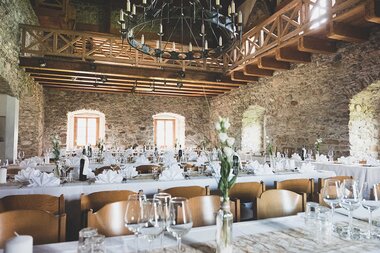 Festively set tables in a rustic castle hall for a wedding with high ceilings and wooden details. | © Burg Kaprun