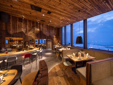 Interior of an elegant restaurant with wooden furniture and large windows offering mountain views. | © Schmittenhöhe