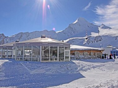 Snow-covered hut in a winter landscape with mountains in the background and clear sunny sky. | © Kitzsteinhorn