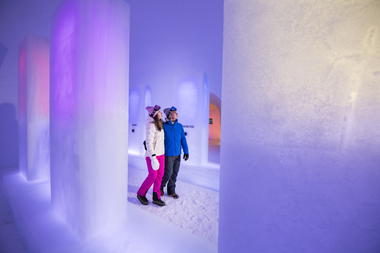 Two people in winter clothing inside an ice cave illuminated with blue and purple lights. | © Kitzsteinhorn