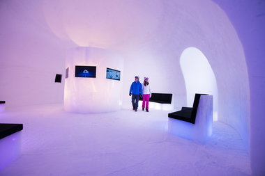 Interior of an ice museum with black padded seating and TV screens, set in a snow-covered environment. | © Kitzsteinhorn