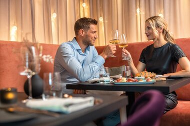 Two people toast with glasses of wine in a restaurant while enjoying food. | © Tauern SPA Zell am See-Kaprun