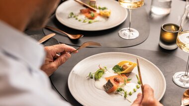 Elegant plated dish at a fine dining setting with wine and water, on a decorated table, contemporary presentation. | © Tauern SPA Zell am See-Kaprun
