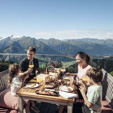 Family dining on a terrace with mountain views at Schmittenhöhe during summer. | © Zell am See-Kaprun Tourismus