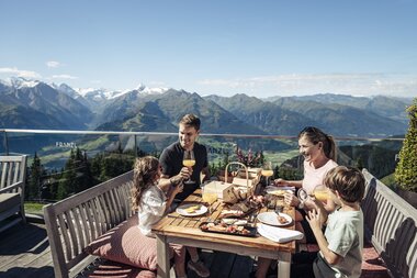 Family dining on a terrace with mountain views at Schmittenhöhe during summer. | © Zell am See-Kaprun Tourismus