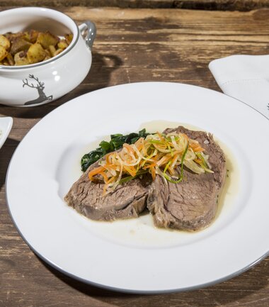 A dish with a piece of meat served with vegetable garnish on a white plate. | © Nikolaus Faistauer Photography