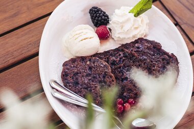 Dessert with chocolate cake, raspberries, blackberry, mint, vanilla ice cream, and whipped cream on a white plate. | © Zell am See-Kaprun Tourismus