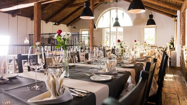 Elegant decorated event space with long tables, candles, flowers, and tableware in a rustic wooden building. | © Klaus Bauer