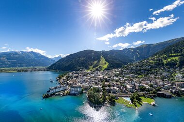 Aerial view of Zell am See, with the lake surrounded by mountains under a sunny sky. | © Nikolaus Faistauer