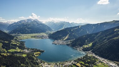 Aerial view of Zell am See and Lake Zell, surrounded by mountains and lush valleys in sunny weather. | © Zell am See-Kaprun Tourismus