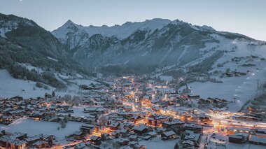 Snowy mountain village at dusk, illuminated by warm street lights in a winter landscape. | © EXPA FEI