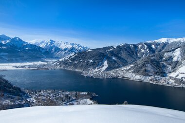 Winter landscape with a view of a lake surrounded by snow-covered mountains and hills. | © Nikolaus Faistauer