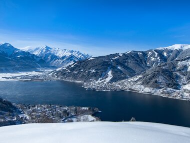 Winter landscape with a view of a lake surrounded by snow-covered mountains and hills. | © Nikolaus Faistauer