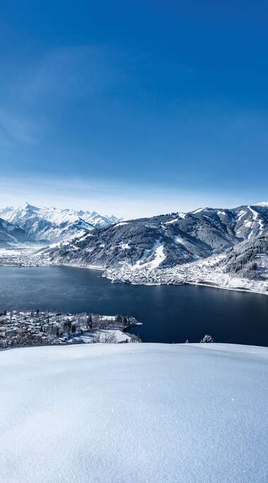 Winter landscape with snow-covered mountains, a lake, and a clear blue sky. | © Nikolaus Faistauer