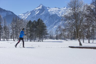 Cross-country skier in snowy landscape with mountains and trees in the background. | © Nikolaus Faistauer Photography