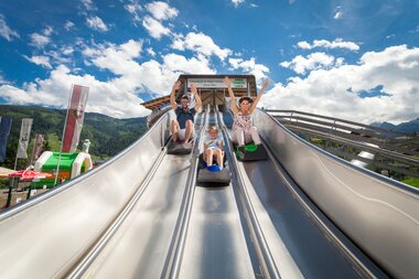 Family sliding at an amusement park with mountains and sky in the background. | © Kitzsteinhorn