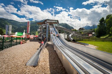 Large outdoor slides under a scenic mountain landscape on a sunny day, part of a water park. | © Kitzsteinhorn