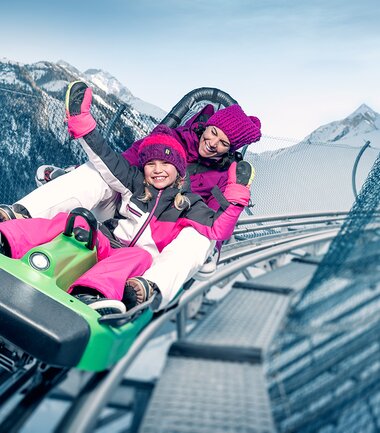 Two children are joyfully riding a toboggan on a snowy mountain slide. | © Kitzsteinhorn
