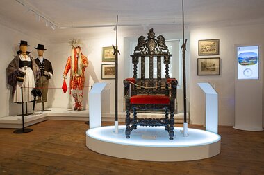 Exhibition with historical clothing and a ornate, antique throne in a museum. | © Peter Brand