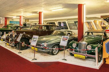 Vintage car models in a museum, displayed on a red carpet with barriers around. | © Vötters Oldtimer Museum