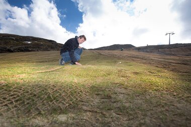 Person measuring the condition of a green hillside on a mountain under cloudy sky. | © Kitzsteinhorn
