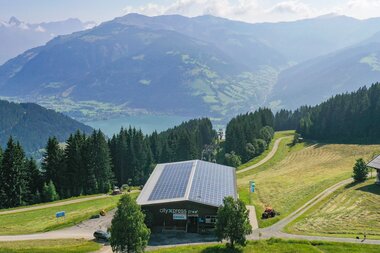 Solar panel installation on a modern building in a lush, mountainous landscape with forests and hills in the background. | © Schmittenhöhe