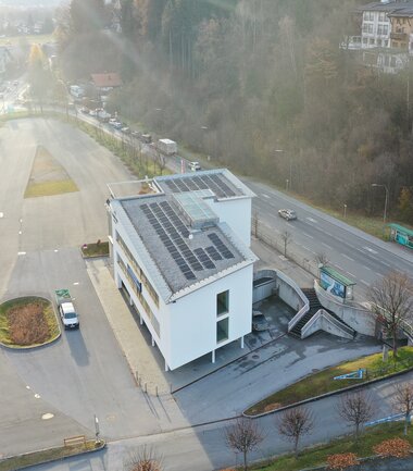An office building with solar panels on the roof, surrounded by a parking lot and street in an urban setting. | © Schmittenhöhe