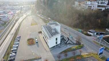 An office building with solar panels on the roof, surrounded by a parking lot and street in an urban setting. | © Schmittenhöhe