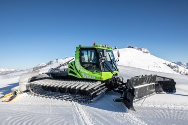 Snowcat in snowy mountain landscape with clear blue sky and snow-covered peaks in the background. | © Nikolaus Faistauer