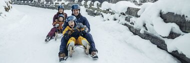 Family sledding on a snowy road in a winter landscape. | © Zell am See-Kaprun Tourismus