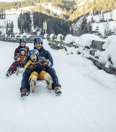 Family sledding on a snowy road in a winter landscape. | © Zell am See-Kaprun Tourismus
