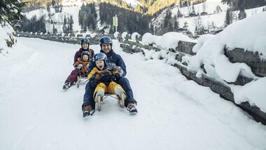 Family sledding on a snowy road in a winter landscape. | © Zell am See-Kaprun Tourismus