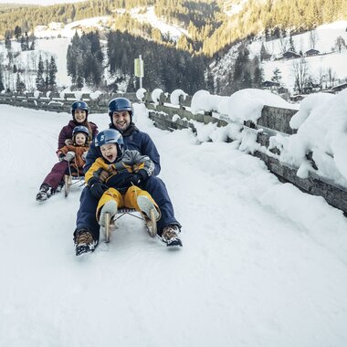 Family sledding on a snowy road in a winter landscape. | © Zell am See-Kaprun Tourismus