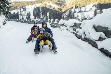 Family sledding on a snowy road in a winter landscape. | © Zell am See-Kaprun Tourismus