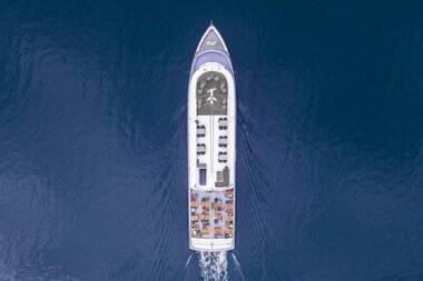 A motorboat is sailing on a lake, viewed from above, surrounded by calm blue water. | © Zell am See-Kaprun Tourismus
