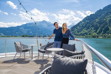 Two people relaxing on a boat with a view of a lake and surrounding mountains. | © Schmittenhöhe, Max Steinbauer