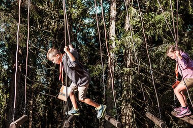 Two children on a rope bridge in the woods, balancing. | © Schmittenhöhe