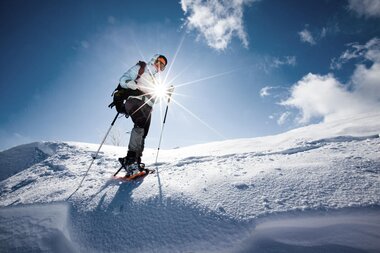 A person snowshoeing on a snowy slope under a clear blue sky with some clouds. | © Kitzsteinhorn