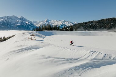Winter scene with snowshoeing in a snowy landscape with mountains in the background. | © Zell am See-Kaprun Tourismus