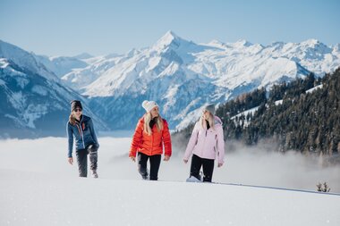 Group hiking in snowshoeing gear through a snowy mountain landscape with high peaks in the background. | © Zell am See-Kaprun Tourismus