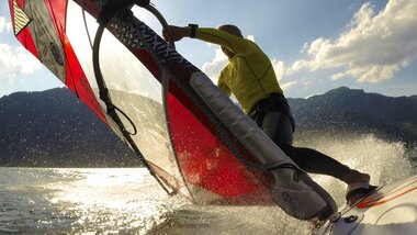Person windsurfing on the water with a sail, mountains in the background. | © Zell am See-Kaprun Tourismus