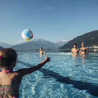 Family enjoying water fun at the outdoor pool with mountain scenery in the background, child playing with a ball in the water. | © Korbinian Seifert